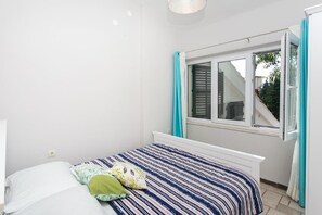 Quarto com cama, janela com cortinas e vista para um edifício.