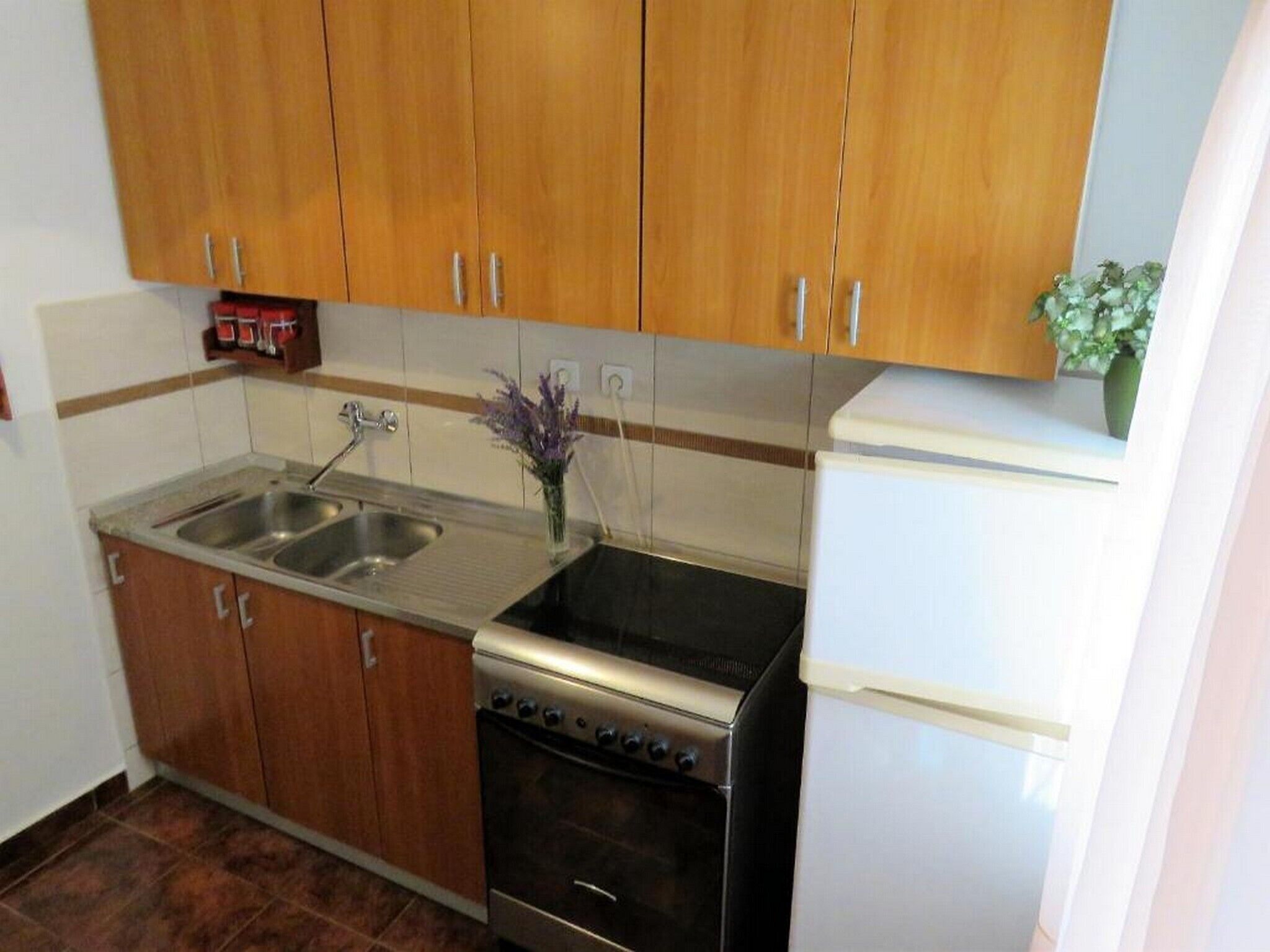 A compact kitchen with wooden cabinets, a stainless steel sink, a stove, and a white refrigerator.