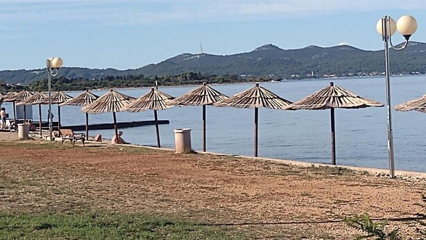 A beach with rows of thatched umbrellas and a row of beach chairs. - Apartments Franica - Three Bedroom Apartment with Terrace (Zadar)