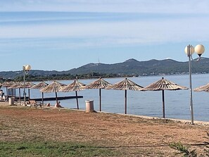 Una playa con hileras de sombrillas de paja y una fila de sillas.
