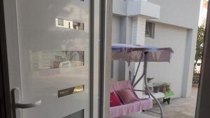 A modern, white-framed glass door with a metal handle, leading to an outdoor area with a concrete floor and a metal swing chair.