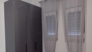 A room with a large wardrobe, two windows with blinds, and a white wall.
