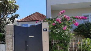 A gated entrance with a number sign, a stone wall, and a building with a tiled roof and balconies.