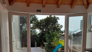A spacious room with a high wooden ceiling and a tiled floor. There is a sliding glass door leading to an outdoor area with a slide and greenery.