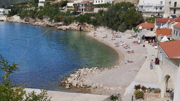 A coastal town with a beach, stone buildings, and a rocky hillside.