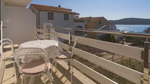 A balcony with a table and chairs, overlooking a body of water and buildings. - Apartment with sea view 1 (Pirovac)