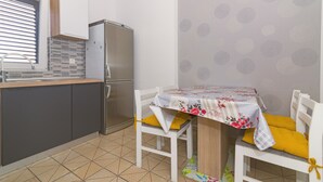 A compact kitchen with a refrigerator, a sink, and a dining area with a table and chairs. - Apartment with sea view 1 (Pirovac)