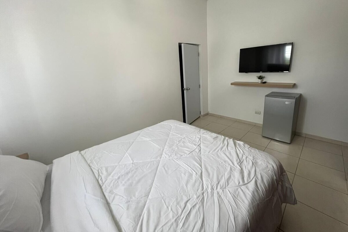 Una camera d'albergo con un letto, una televisione, un mini-frigorifero e una porta.