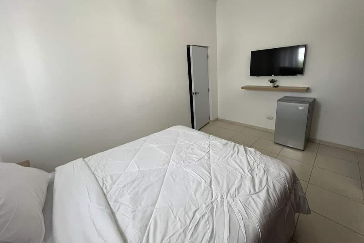 Une chambre à coucher avec un lit, un téléviseur fixé au mur et un petit réfrigérateur.