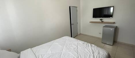 A bedroom with a bed, a television mounted on the wall, and a small refrigerator.