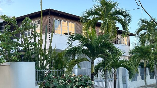 A two-story house with a balcony, surrounded by palm trees and a white fence. - El Montserrat - Hotel Boutique (Santiago de los Caballeros)
