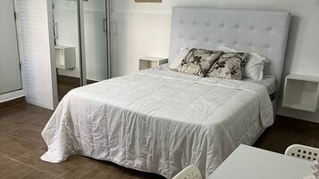 A bedroom with a bed, a white table, and chairs.