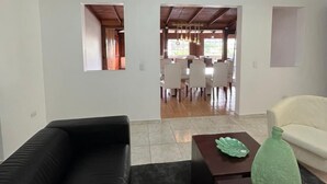 A living room with a black sofa, a white sofa, and a dining area in the background. - El Montserrat - Hotel Boutique (Santiago de los Caballeros)