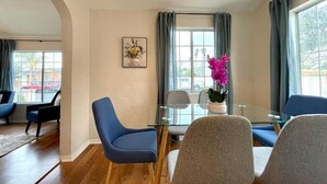 A modern room with a glass dining table, blue and grey chairs, a potted plant, and a framed picture on the wall.