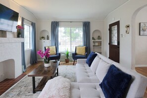 A living room with a fireplace, a sofa, a coffee table, and a television. - Extraordinaire Casa 2B1B KING beds (Long Beach)