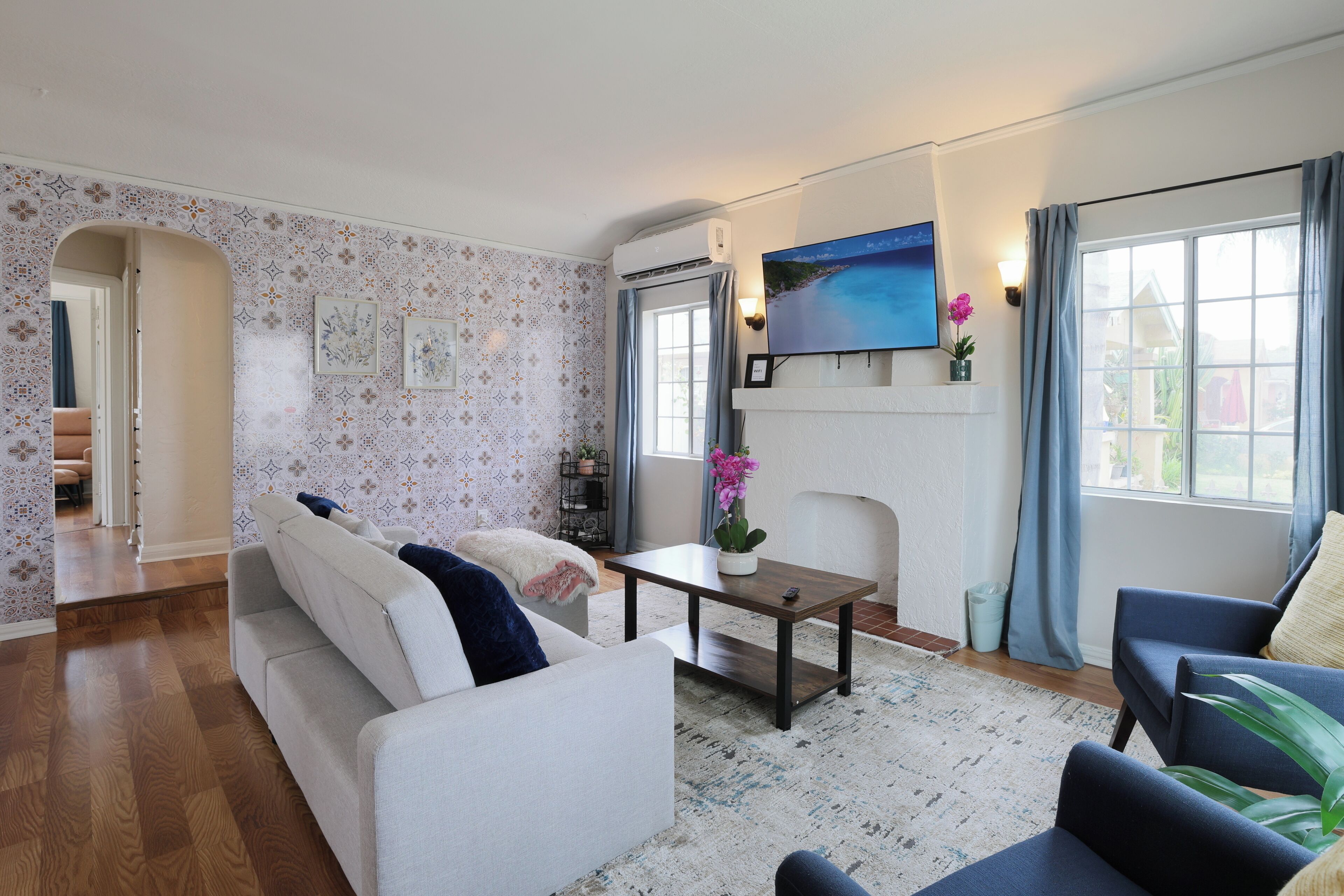 A living room with a sofa, armchairs, a coffee table, and a TV mounted on the wall.