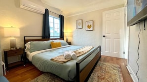 A bedroom with a bed, bedside lamps, a window with curtains, a door, and a television on the wall.