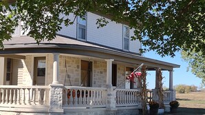 Une maison à deux étages avec un porche, des colonnes en pierre et un drapeau.