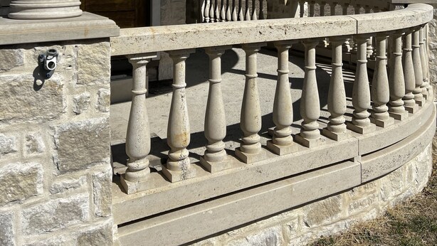 Un porche en pierre agrémenté d’une balustrade, une porte en bois et une vue dégagée sur le paysage.