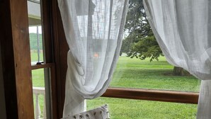 Une fenêtre avec des rideaux blancs, un banc rembourré et une vue sur un paysage verdoyant.