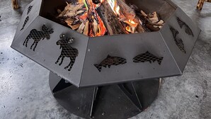 Una habitación acogedora con una chimenea central que presenta siluetas de animales, muebles de madera y ventanas amplias que ofrecen vistas al exterior.