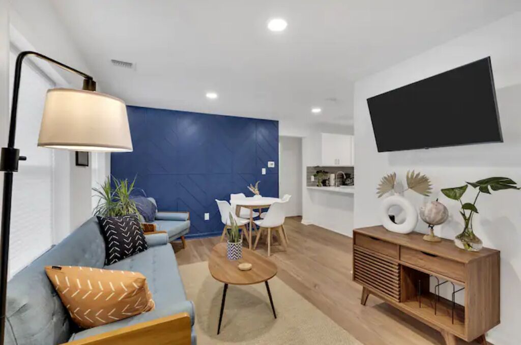 A modern living room with a sofa, a coffee table, a dining area, and a TV mounted on the wall.