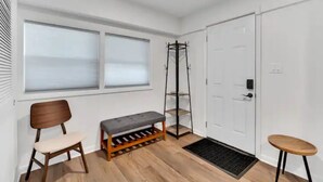 Ein Zimmer mit einer Bank, einem Stuhl, einem Kleiderhaken und einer Tür.