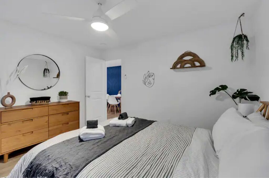 A bedroom with a bed, a dresser, a mirror, and a hanging plant.