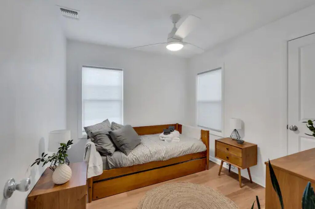 Un dormitorio con cama de madera, mesitas de noche, ventilador de techo y ventanas amplias.