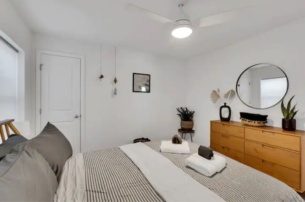 Un dormitorio con cama, cómoda, espejo, ventilador de techo y puerta.