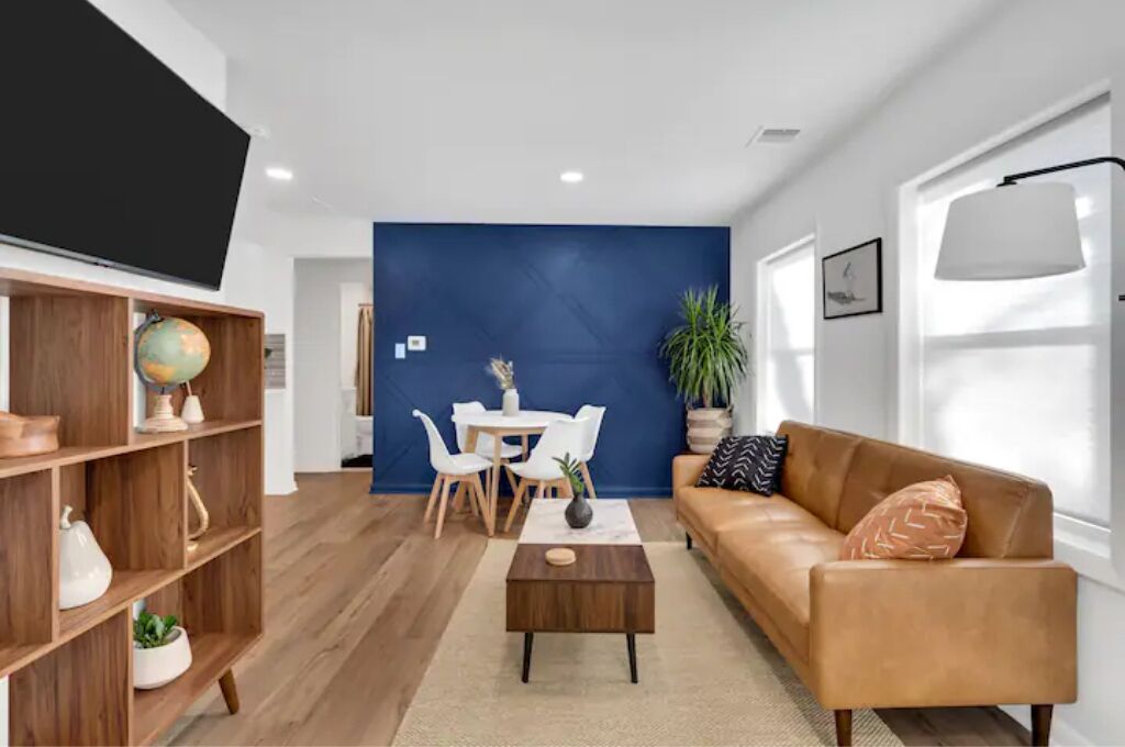 Una sala de estar moderna con una pared de acento azul, un sofá de cuero, una mesa de centro, una estantería y un televisor de pantalla plana.