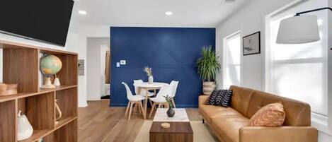 Una sala de estar moderna con una pared de acento azul, un sofá de cuero, una mesa de centro, una estantería y un televisor de pantalla plana.