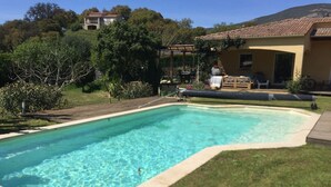 A rectangular swimming pool with a tiled edge, surrounded by a grassy area and a wooden deck. - A cozy and well-located chalet. (APPIETTO)