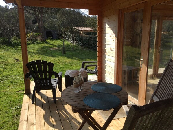 A wooden deck with a table and chairs, a glass door, and a view of a grassy yard with trees.
