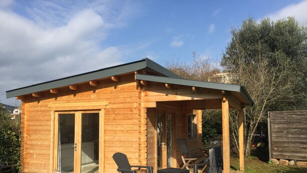 A wooden cabin with a covered patio, a sliding glass door, and outdoor seating. - A cozy and well-located chalet. (APPIETTO)