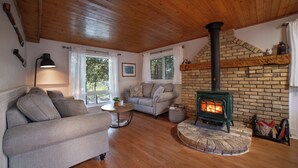 A cozy living room with a fireplace, wooden floors, and a sofa. - Charming Cottage on the River (South Bruce Peninsula)