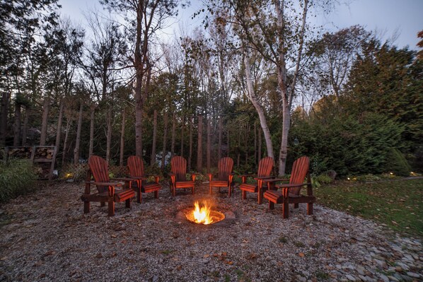 A circular seating arrangement around a fire pit in a forested area. - Charming Cottage on the River (South Bruce Peninsula)