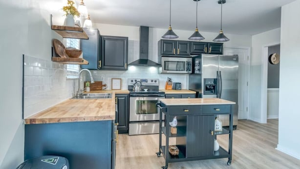 A modern kitchen with dark cabinetry, stainless steel appliances, and a wooden island.