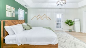 A bedroom with a bed, a wooden headboard, a green wall, a white door, and a plant.