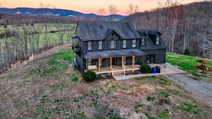 A large, two-story log cabin with a porch and a covered front deck, surrounded by open fields and trees.
