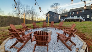 An outdoor seating area with Adirondack chairs arranged around a fire pit, surrounded by gravel and a wooden border.