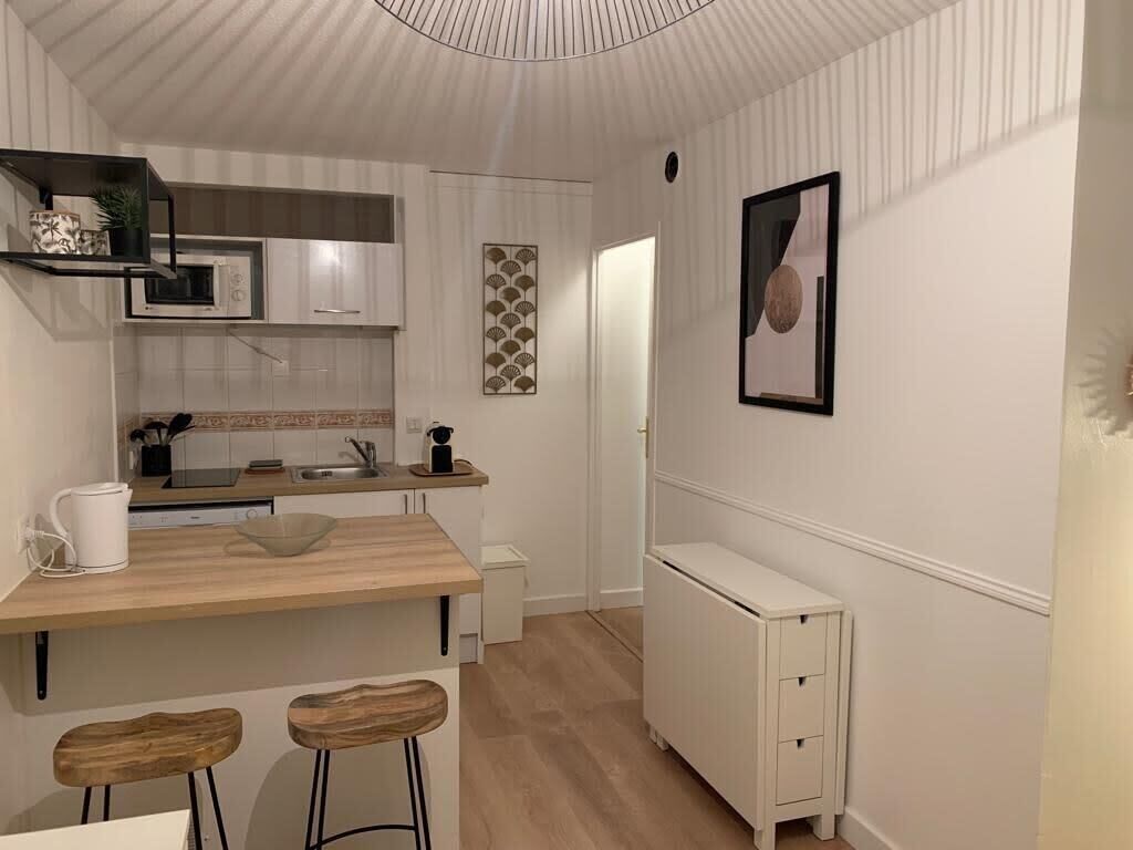 Una cucina compatta con un piano di lavoro in legno, mobili bianchi e una piccola isola con sgabelli.