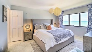 A bedroom with a bed, bedside tables, a nightstand, a window with a view, and a door. - Lovely Fort Pierce Condo, Walk to Beach! (Fort Pierce)