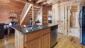 Interno di una baita in legno con cucina, zona pranzo e una scala.