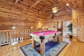 Un intérieur en bois avec une table de billard, un ventilateur de plafond et une plante en pot.