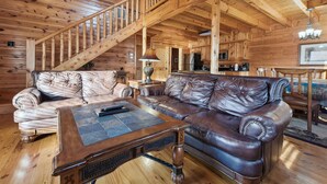 Interno di una baita in legno con una scala in legno, divani in pelle, un tavolino da caffè in legno e una zona cucina.