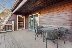 A wooden deck with a glass door leading to a room with a bed. There are four wicker chairs and a round table on the deck.