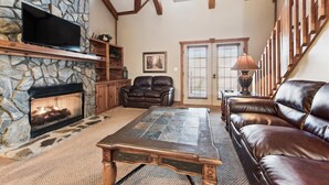 A cozy living room with a stone fireplace, leather furniture, and a wooden ceiling.