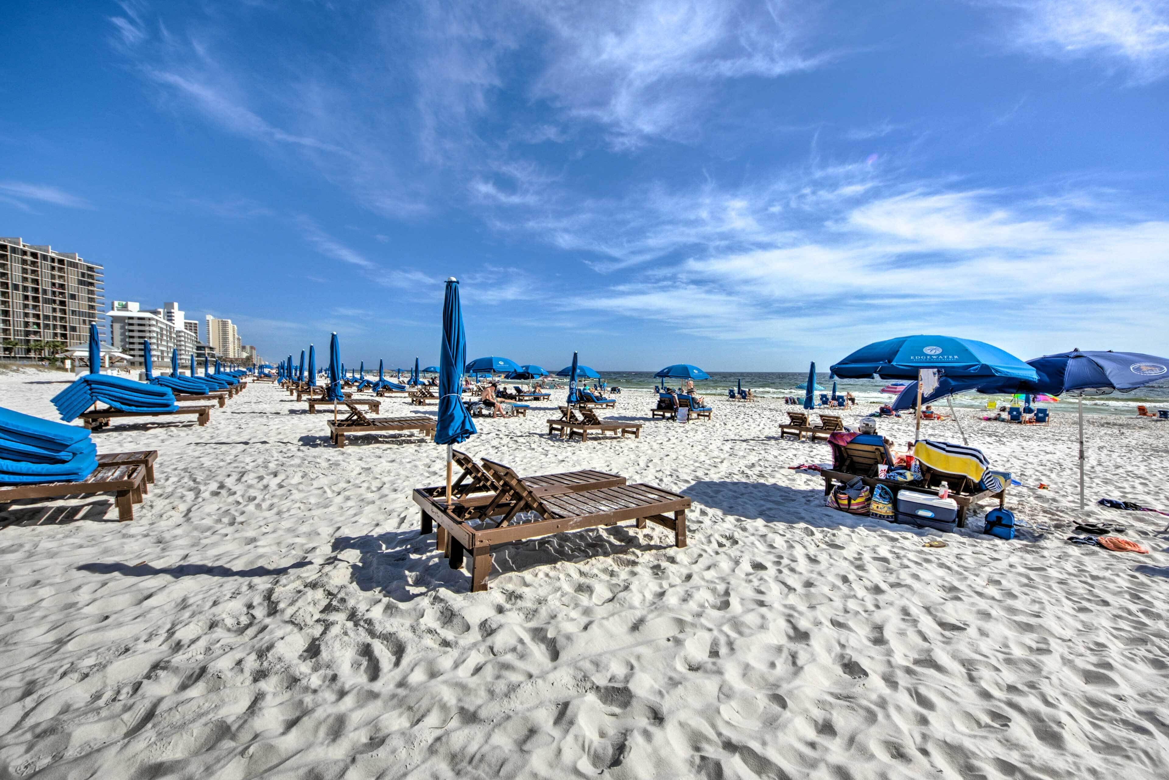 A beach with rows of wooden lounge chairs and blue umbrellas, some with bags and items on them.