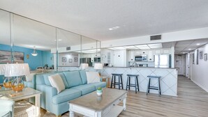 A modern living room with a light blue sofa, a coffee table, and a kitchen area with a bar counter. - PCB Vacation Rental w/ Sweeping Ocean Views! (Panama City Beach)